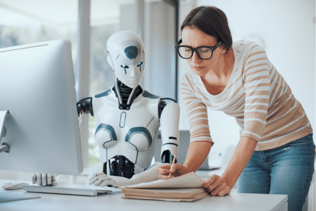 uporaba-ai-v-hrm Ženska skupaj z robotom uporablja računalnik pri administrativnem delu.